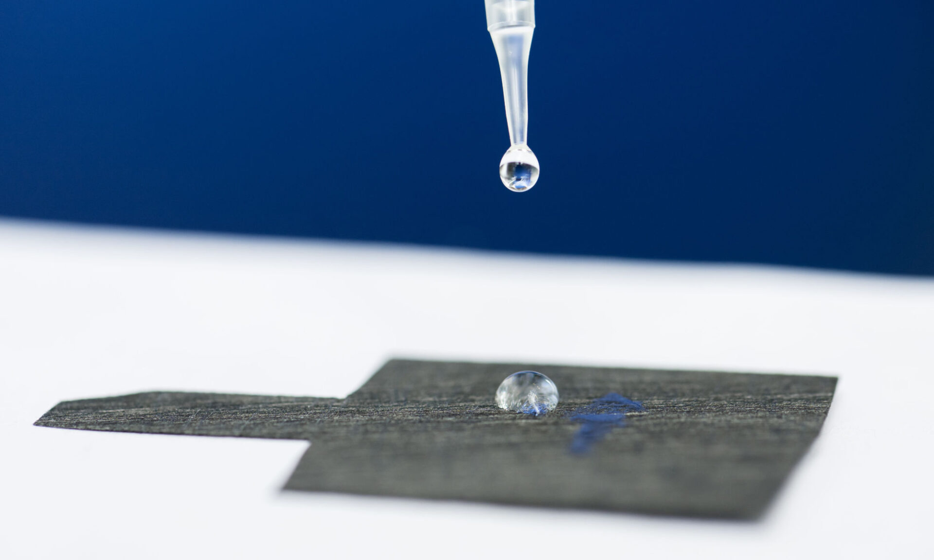 Pipette releasing a water droplet atop carbon paper to illustrate pfas chemical remediation.